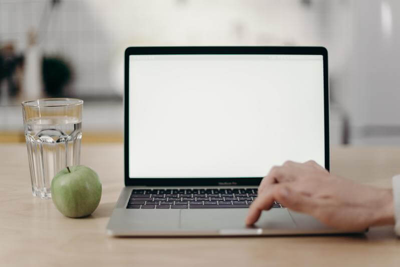 Foto de un ordenador portátil junto a un vaso y una manzana, y una mano manejando el touchpad